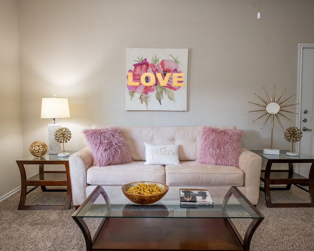 A living room with a white couch, a glass coffee table, and a painting with the word "LOVE" on it.