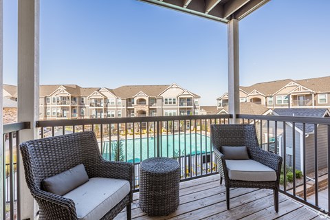 A balcony with two chairs and a table overlooking a pool.
