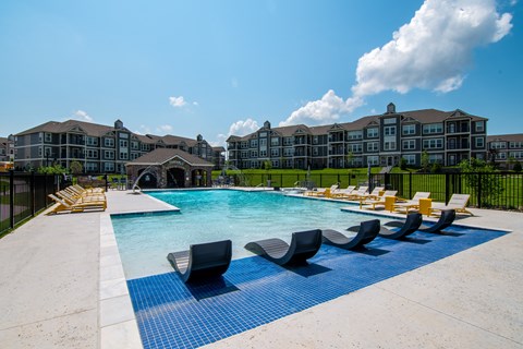 A large swimming pool with lounge chairs in front of a multi-story building.