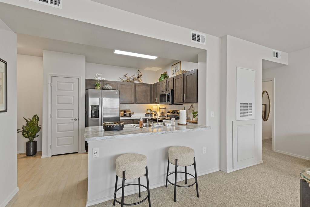 A kitchen with white cabinets and a bar area with two stools.