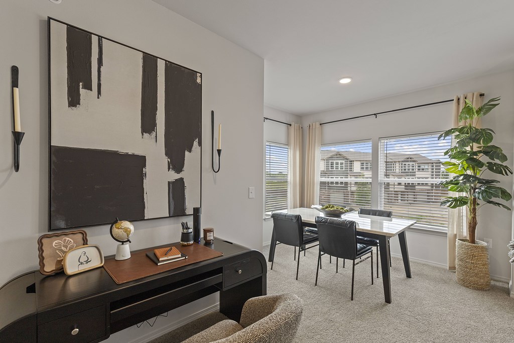 A black and white abstract painting hangs on a white wall above a dark wood desk with a chair and a potted plant.