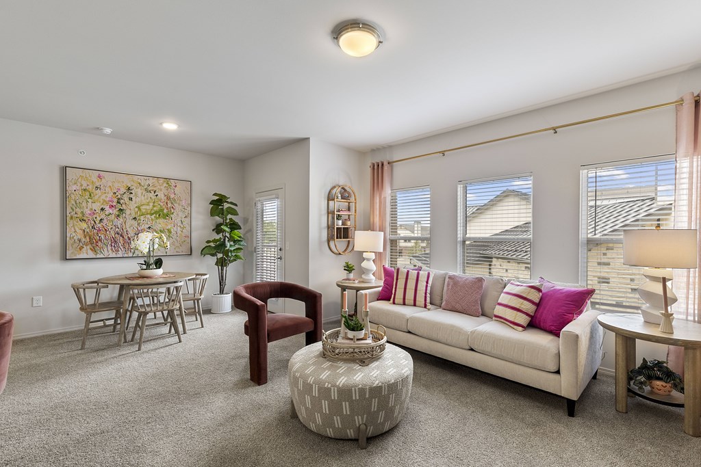 A living room with a white couch, a grey ottoman, a dining table with chairs, and a painting on the wall.