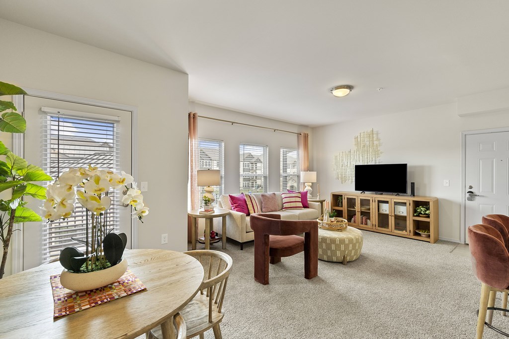 A living room with a wooden table and chairs, a television, and a potted plant.