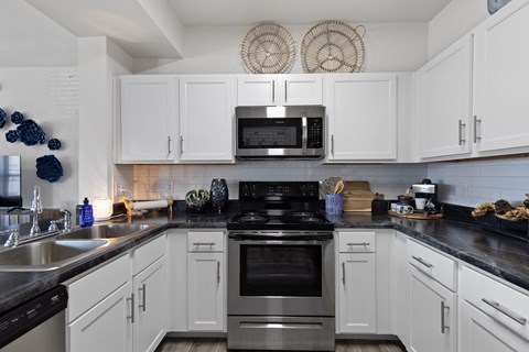 A modern kitchen with white cabinets and black countertops.