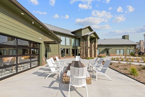 A patio with white chairs and a table in front of a green house.