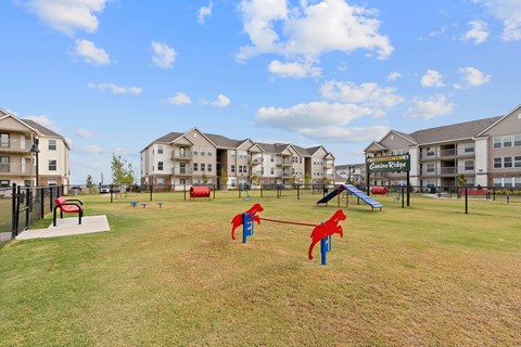 A playground with a slide and a red dog-shaped swing set in front of apartment buildings.