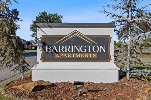A sign for Barrington Apartments is displayed in front of some trees.