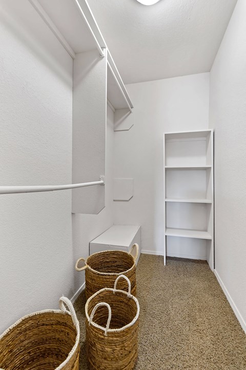 Three wicker baskets are on the floor of a white room with a shelf and a bench.
