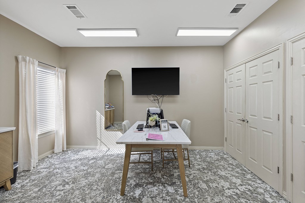 A room with a table, chairs, and a television mounted on the wall.