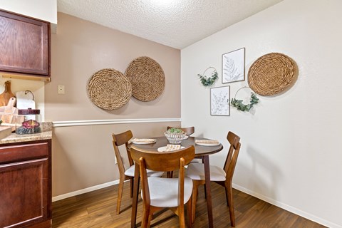 A dining room with a table set for two and a kitchen area with a sink and cabinets.