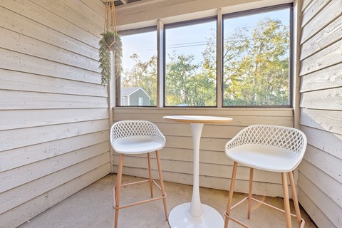 Two white chairs and a table are placed in a room with a window.