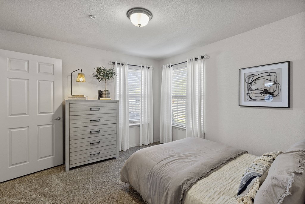 A bedroom with a bed, dresser, and window with curtains.