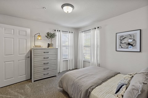 A bedroom with a bed, dresser, and window with curtains.