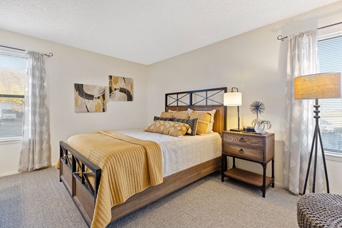 A bedroom with a large bed, a nightstand, and a window with curtains.