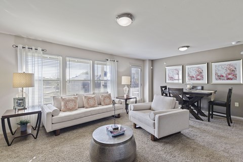 A living room with a white couch, a grey armchair, a coffee table, and a dining table with chairs.