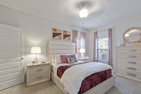 A bedroom with a large bed, a nightstand with a lamp, and a dresser with a mirror.