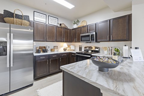 A kitchen with a marble counter top and dark brown cabinets.