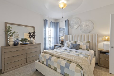 A bedroom with a bed, nightstand, and a dresser with a mirror and decorative items.