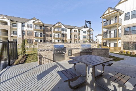 A large outdoor picnic table is in front of apartment buildings.