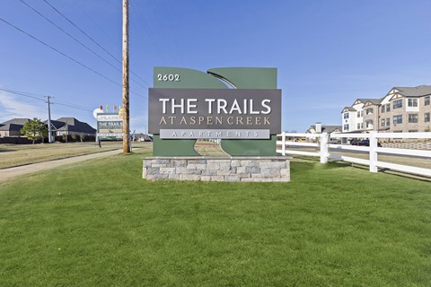 A sign for The Trails at Aspen Creek Apartments stands in a grassy field.