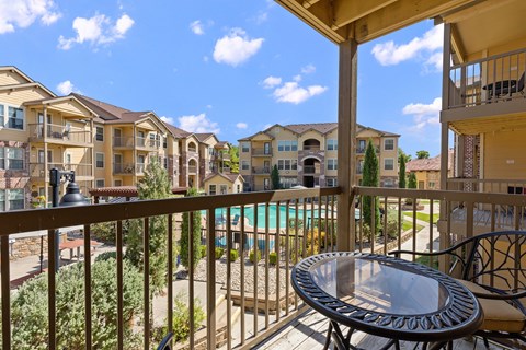 A balcony with a table and chairs overlooks a pool and apartment buildings.