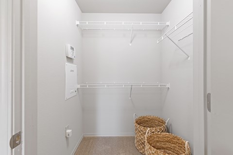 A white closet with a shelf and two baskets on the floor.