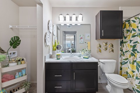 A bathroom with a white toilet, sink, and a shower curtain with a leaf pattern.