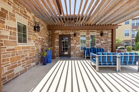 A patio with a wooden pergola and blue cushioned chairs.