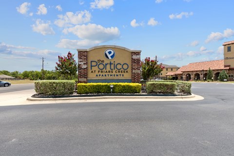 The sign for The Portico at Friars Creek Apartments is displayed in front of a building.