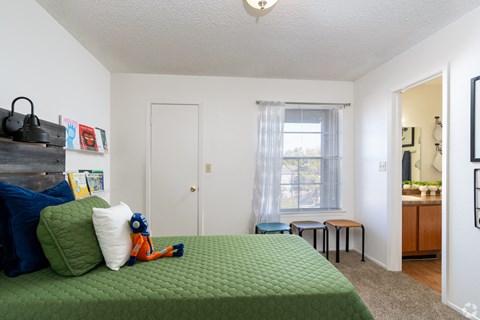 A bedroom with a green bedspread and a window with curtains.