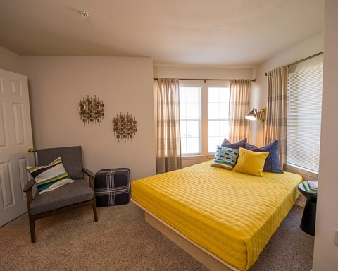 A bedroom with a yellow bed and a grey chair.