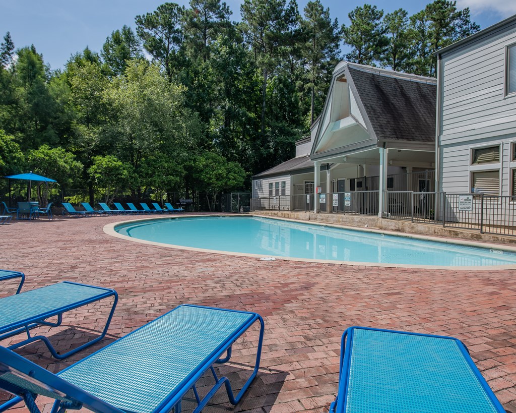 A pool surrounded by blue lounge chairs and a house in the background.