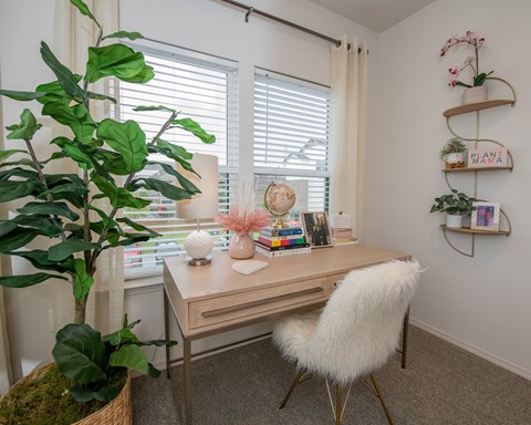 A room with a desk, chair, and a potted plant.