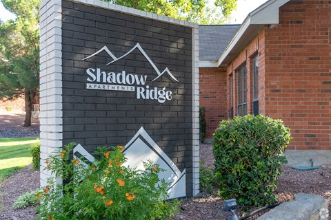 A sign for Shadow Ridge Apartments is displayed in front of a brick building.