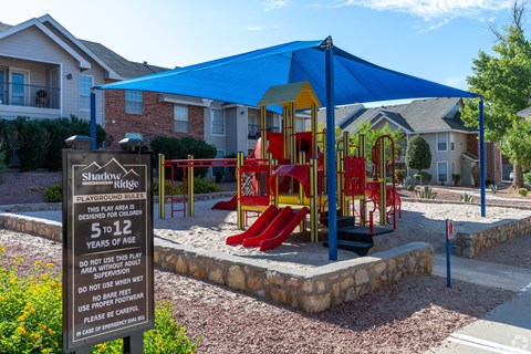 A playground with a blue canopy and a sign that states the playground rules.