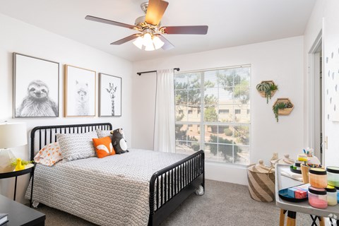 A bedroom with a bed, a ceiling fan, and pictures on the wall.