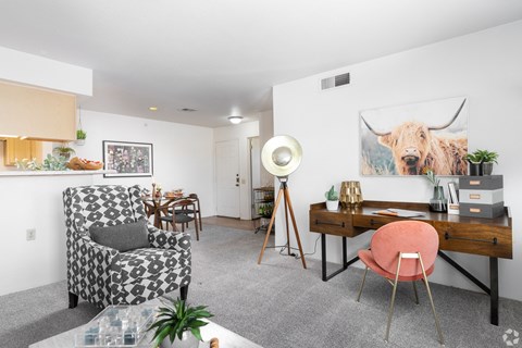 A living room with a patterned chair, a desk with a pink chair, and a painting of a bull on the wall.