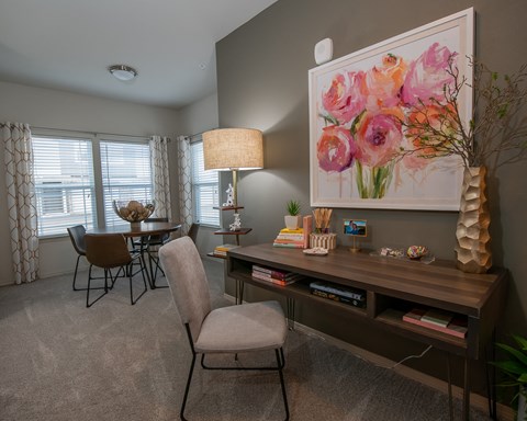 A room with a desk, chair, and a painting of flowers on the wall.
