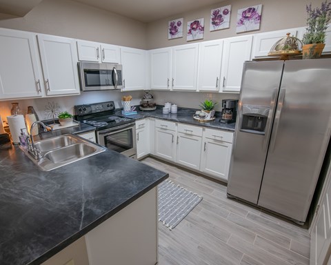 A kitchen with a black counter top and stainless steel appliances.