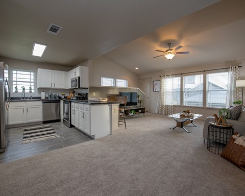 A spacious kitchen and living room with a grey carpet.