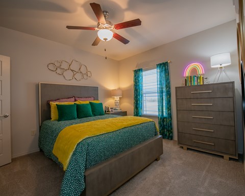 A bedroom with a bed, dresser, and ceiling fan.