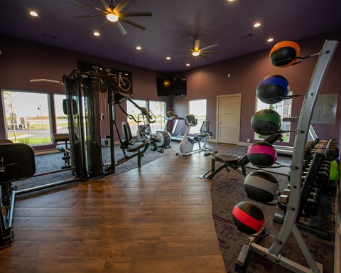 A gym with a variety of equipment including a weight rack, a rowing machine, and a wall mounted pull up bar.