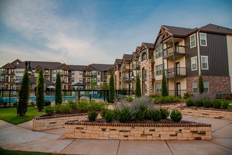 A row of apartment buildings with a pool and landscaping in the foreground.