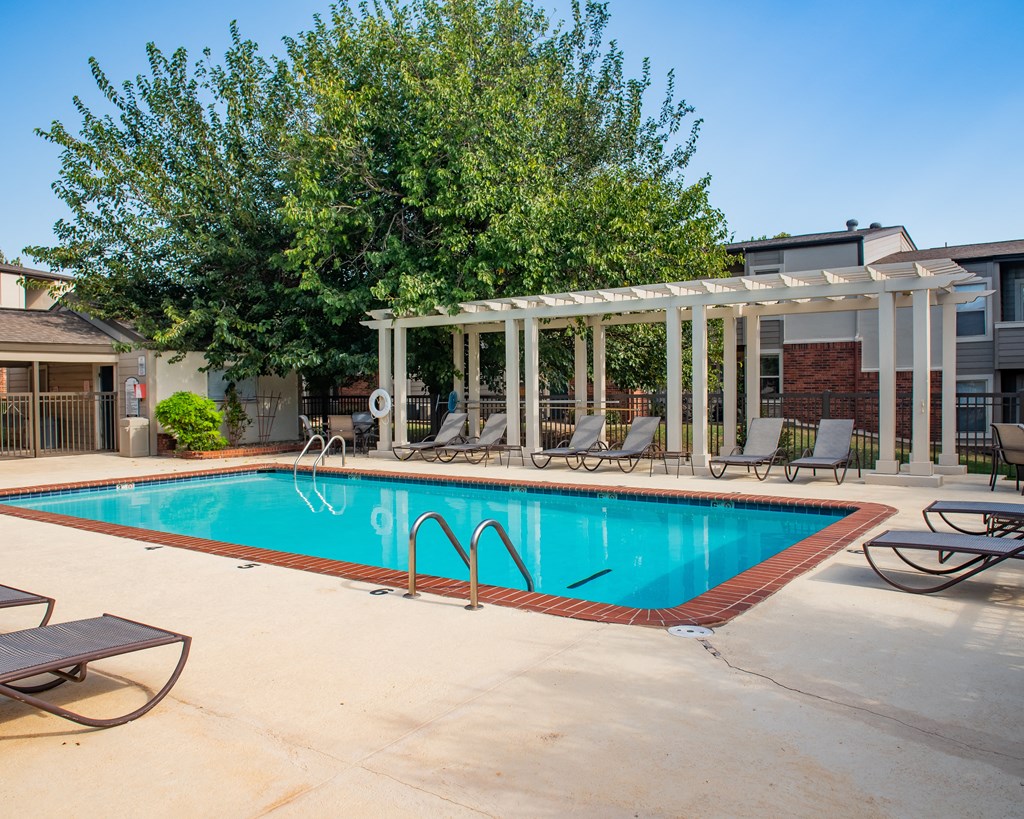 A pool with a white pergola and chairs around it.