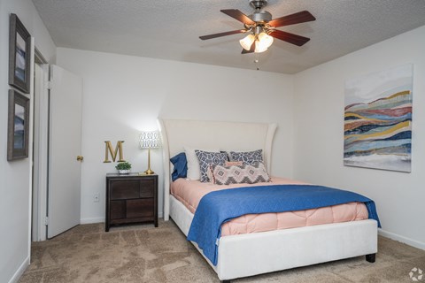 A bedroom with a bed, a ceiling fan, and a painting on the wall.