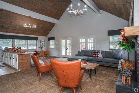 A living room with a grey couch, orange chairs and a wooden ceiling.