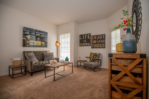 A living room with a grey couch, a coffee table, and a wooden shelf with a vase on top.