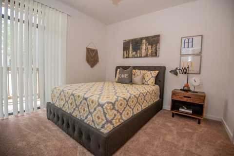 A bedroom with a large bed and a small table with a clock on it.