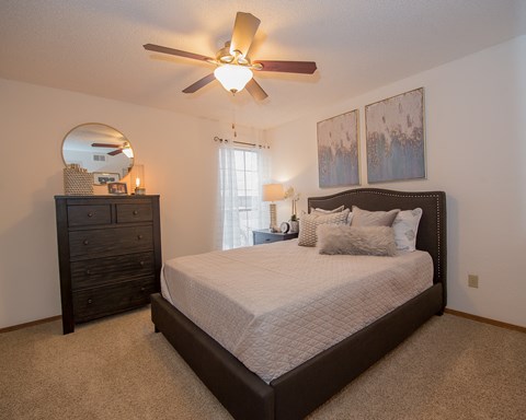 A bedroom with a large bed, a dresser, and a ceiling fan.