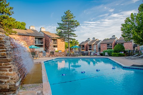 A pool with a waterfall and a building in the background.